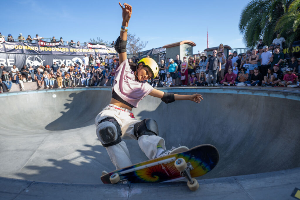 Teen girl skateboarding at an event with lots of people in the background 