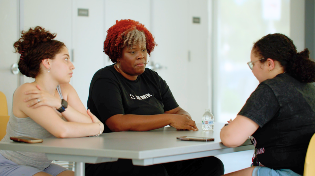 a coach and two young people seated round a table talking 